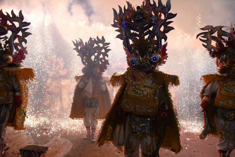 Performers in elaborate costumes march amid a shower of sparks.