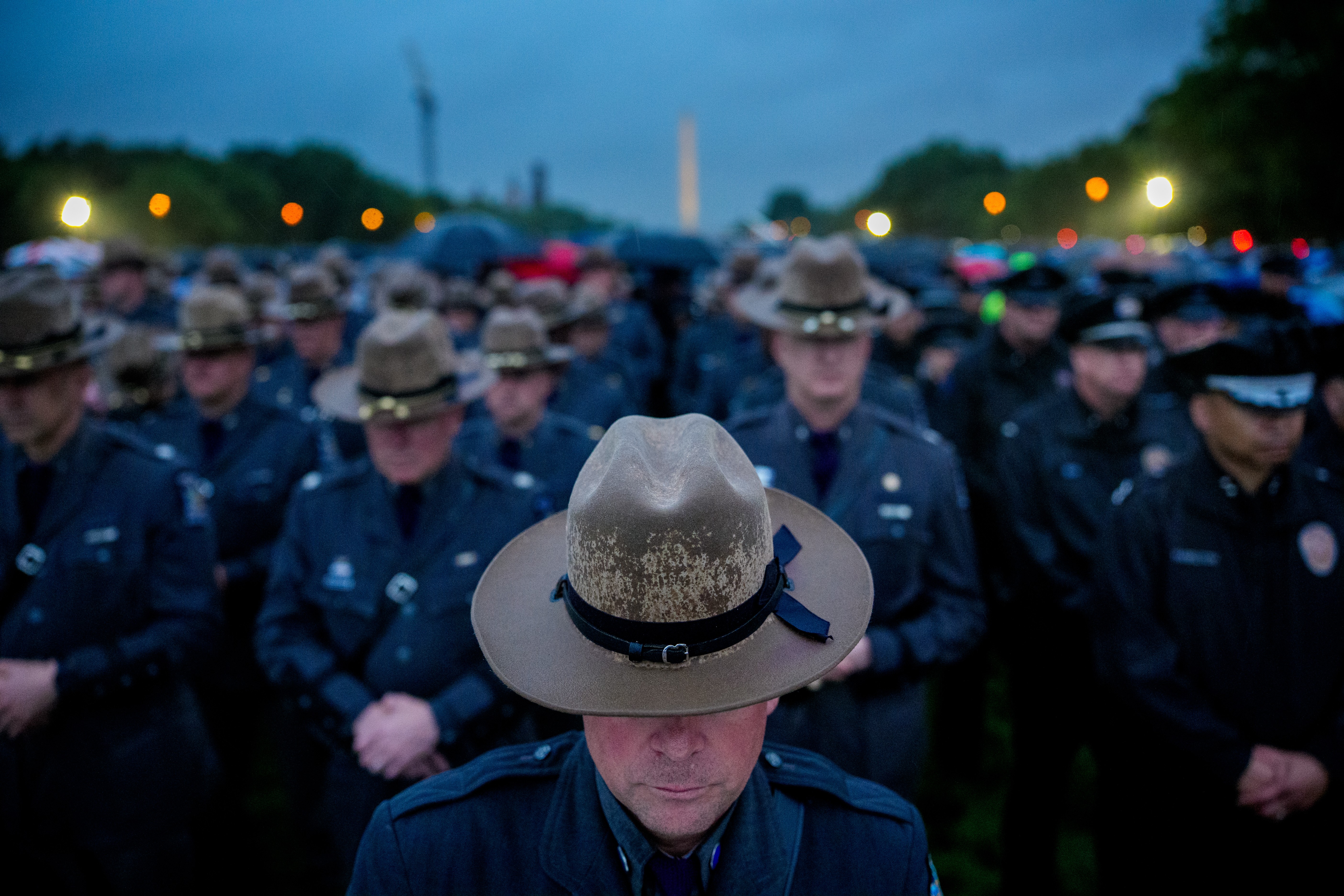 Many police officers stand together, heads bowed, during a vigil.