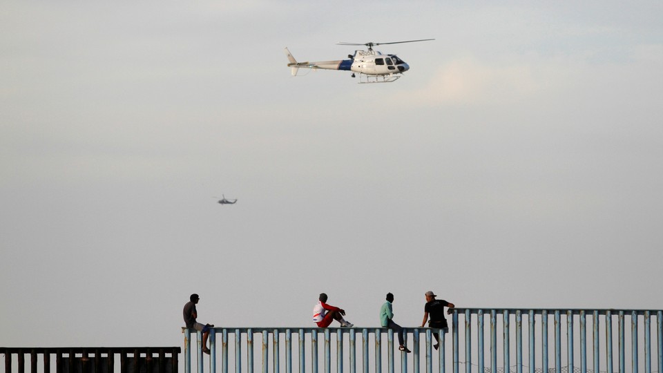 Immigrants sit on a border fence between the United States and Mexico after arriving as part of a caravan.