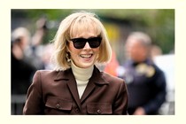 Photo of E. Jean Carroll wearing sunglasses, a white turtleneck, and a brown jacket