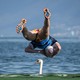 A rugby player leaps from a floating pitch into a lake; a swan in the distance appears to be right under him.