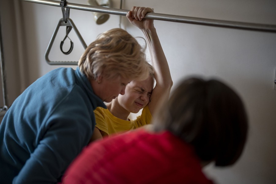 A patient in a hospital holds onto a bar while others help them during a rehabilitation session.