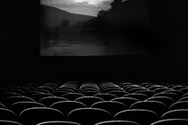 A black and white image of an empty movie theatre with a scenic location on screen