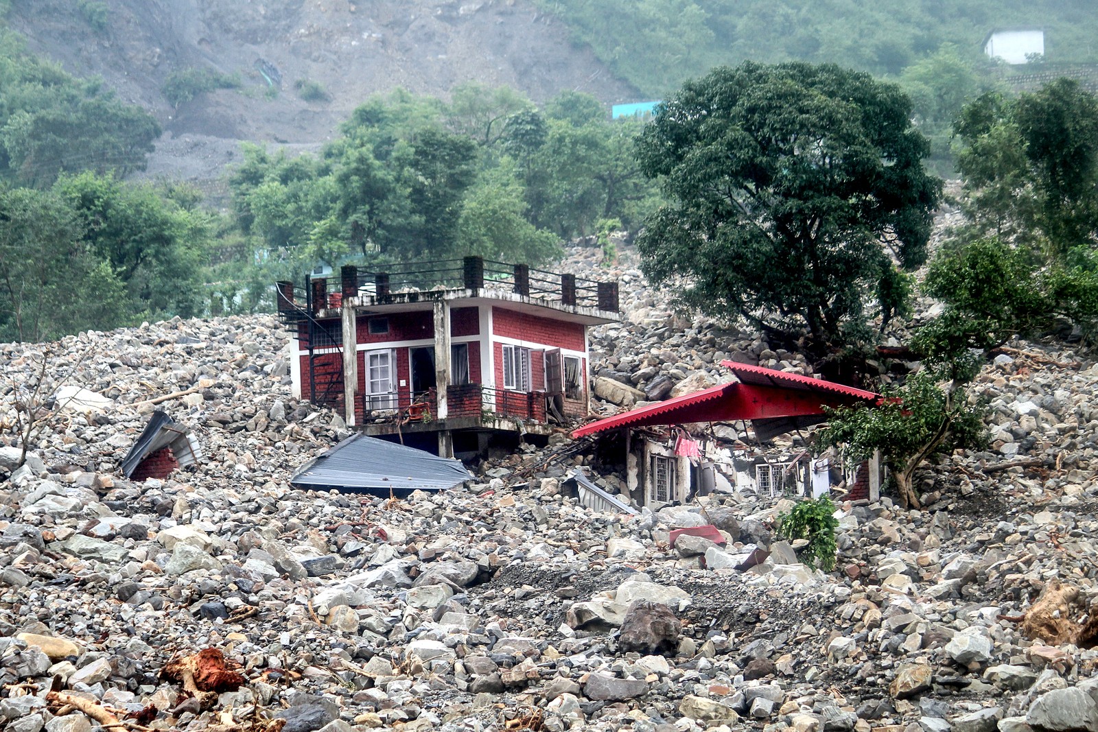 A heavily damaged residential building stands surrounded by rocks after a flood swept through the area.