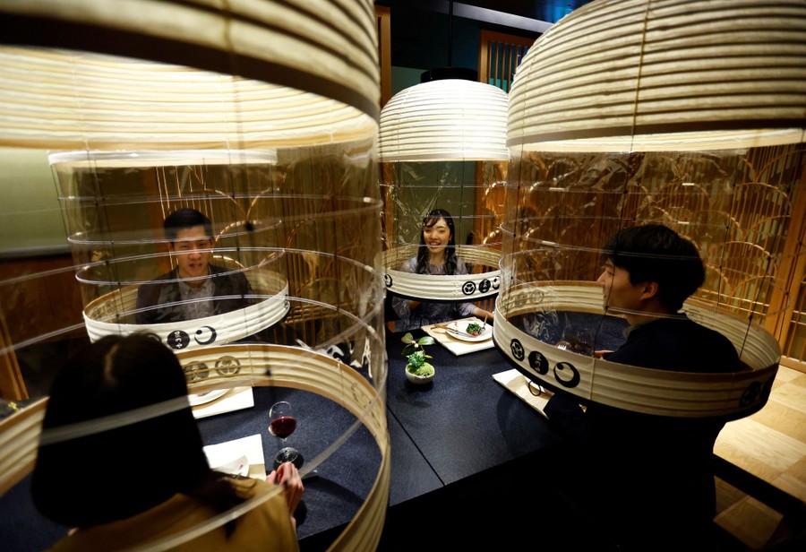 Four people sit at a table, each of them under a transparent, lantern-shaped dome.