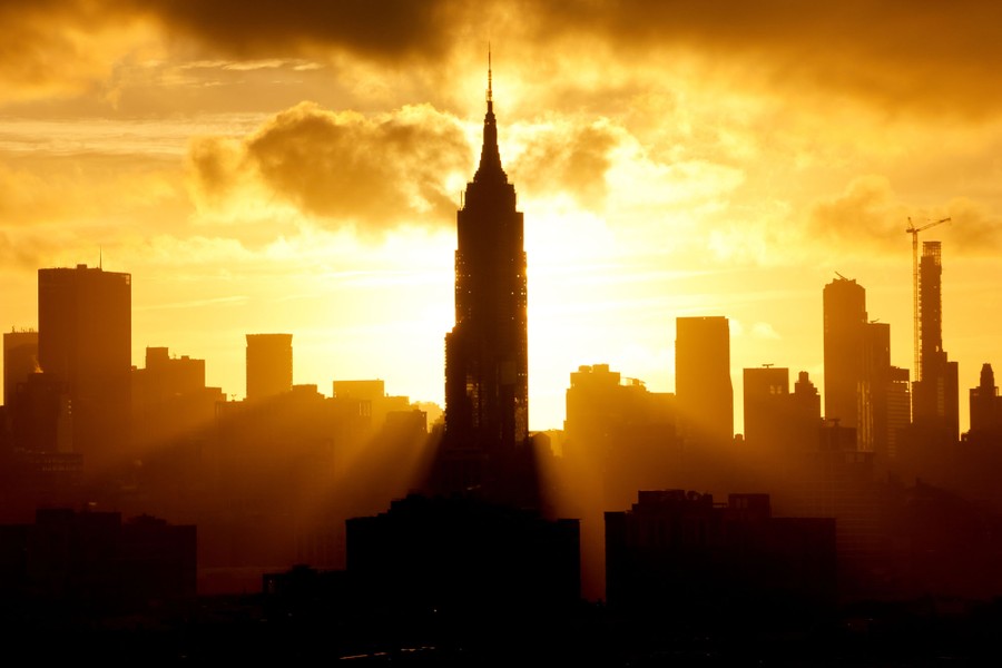 The sun rises behind the skyline of midtown Manhattan and the Empire State Building.