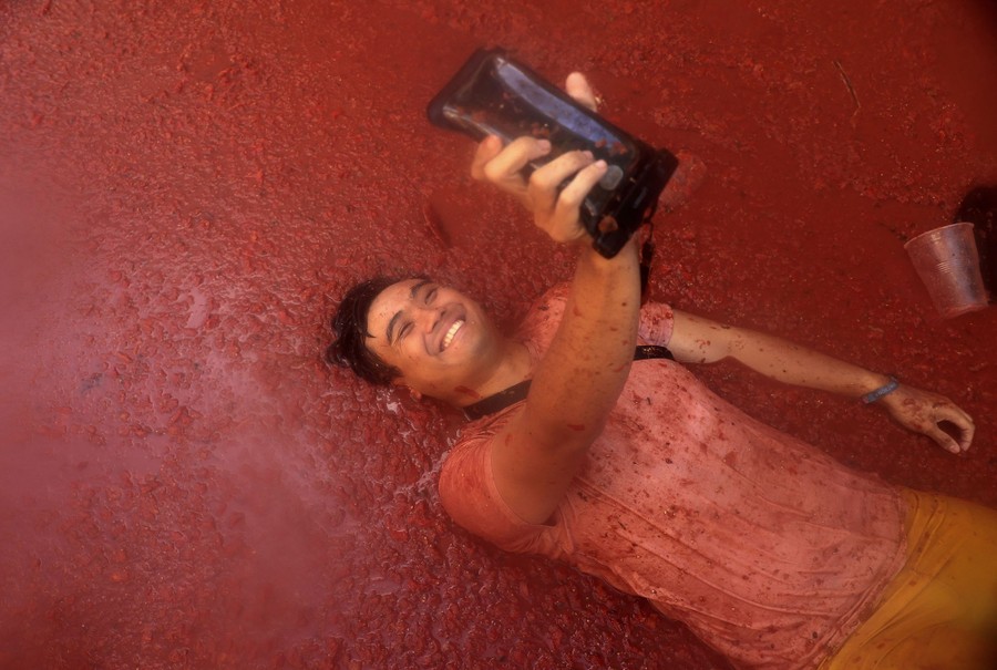 A person takes a selfie while lying down in a pile of crushed tomatoes.