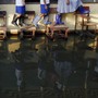 Students wearing rain boots walk on desks across their flooded classroom.