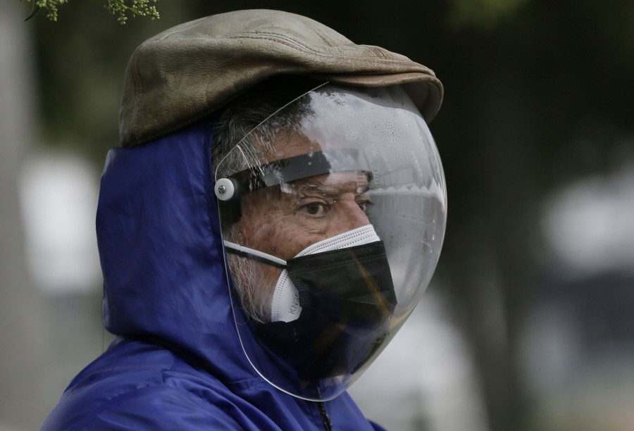 A man wearing a full protective face shield and double mask waits for a vaccination outside.