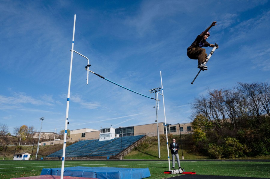 A person leaps very high on a pogo stick, as a judge looks on.