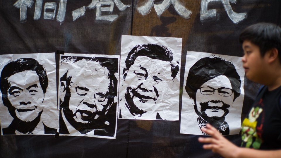 A man walks past a banner with pictures depicting the former Hong Kong chief executives Leung Chun-ying and Tung Chee-Hwa, as well as Chinese President Xi Jinping and Hong Kong Chief Executive Carrie Lam, during an annual National Day prodemocracy rally.