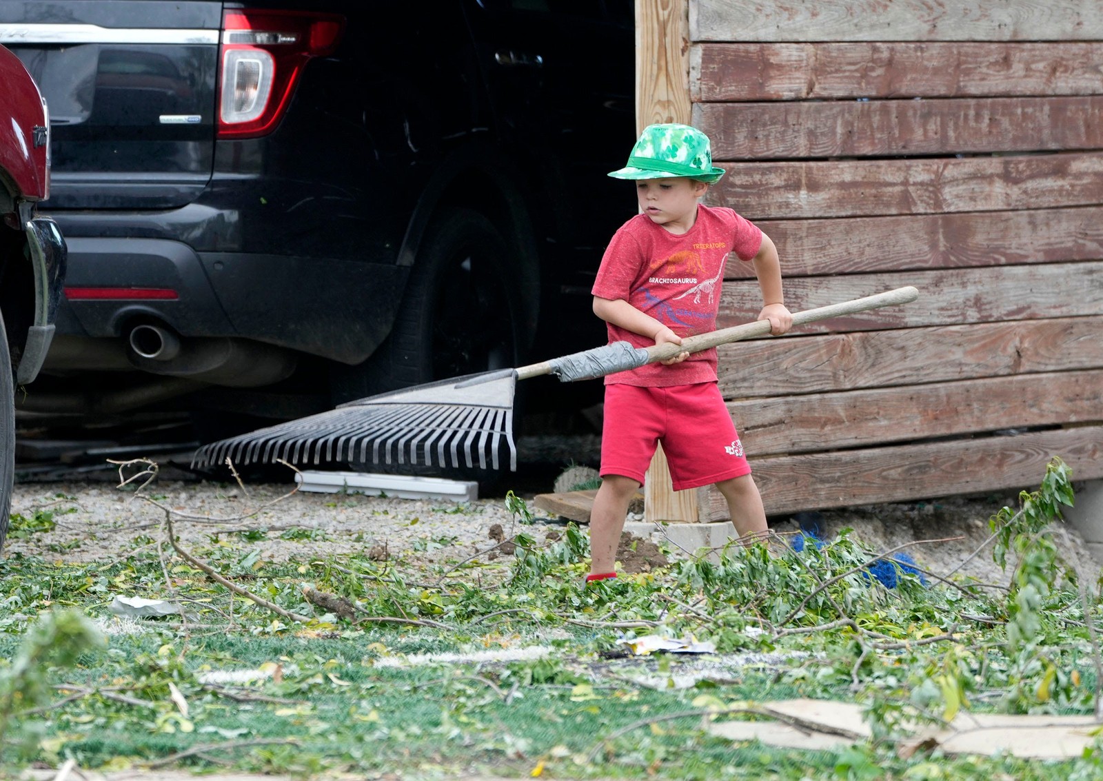 A young boy works to rake up sticks and leaves after a storm.