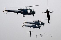 Four soldiers dangle from cables beneath flying helicopters.