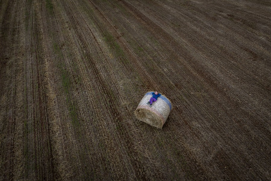 A girl rests on a large, round bale in a field, captured from above.