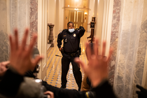 Foto del agente de policía del Capitolio Eugene Goodman parado en la entrada de las escaleras del edificio del Capitolio el 6 de enero de 2021, con la mano levantada, frente a una multitud de alborotadores.