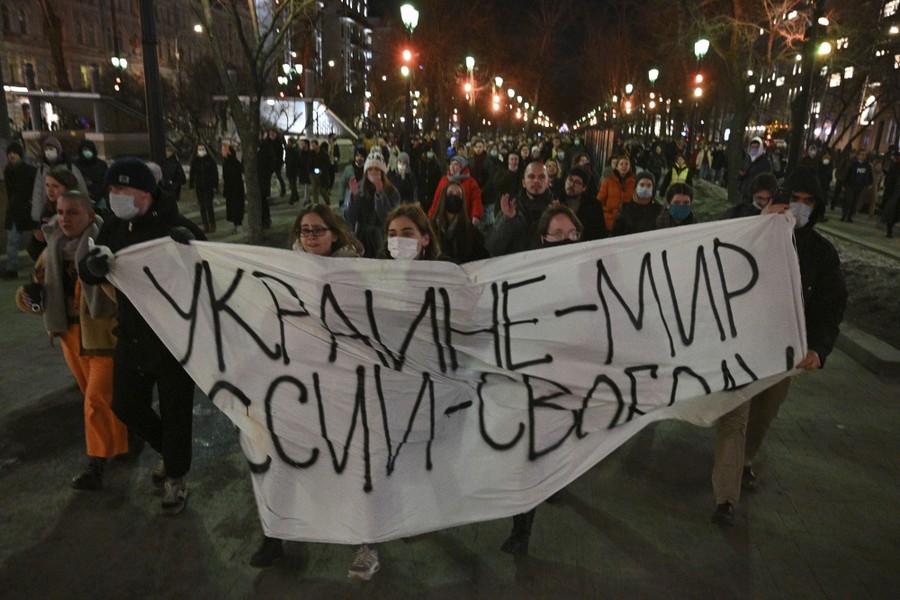 Dozens of people are seen marching in a city street behind a hand-made banner reading (in Russian) "Ukraine—Peace, Russia—Freedom".