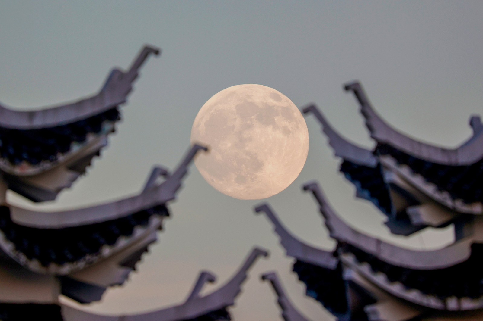 An image of the full moon behind curved pagoda roof edges