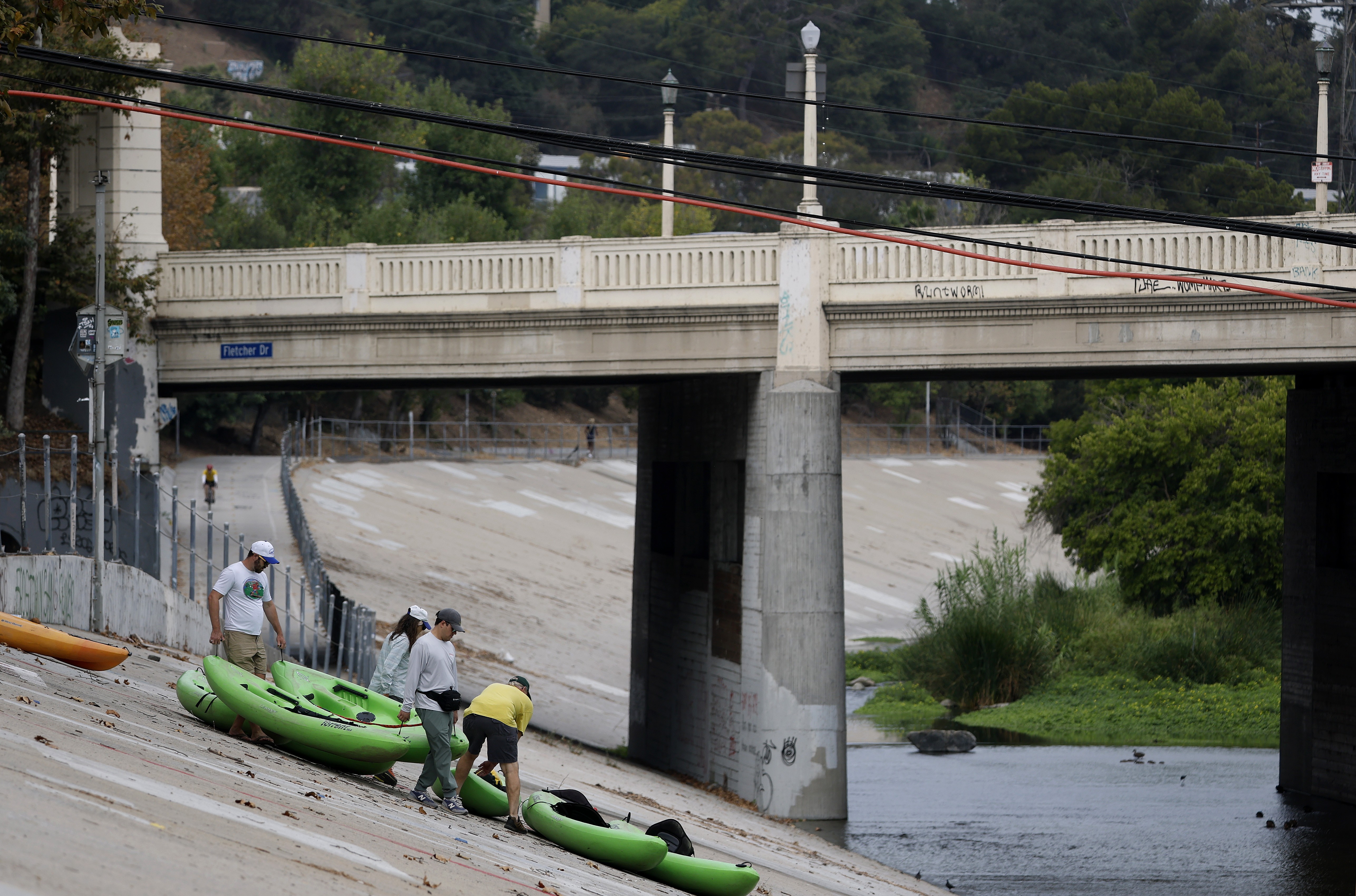 People carry kayaks down a concrete slope into an urban river.