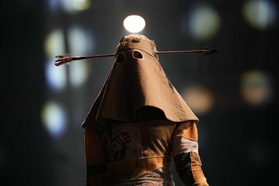 A model wears a head covering with pieces of decor attached that look like an arrow through their head.
