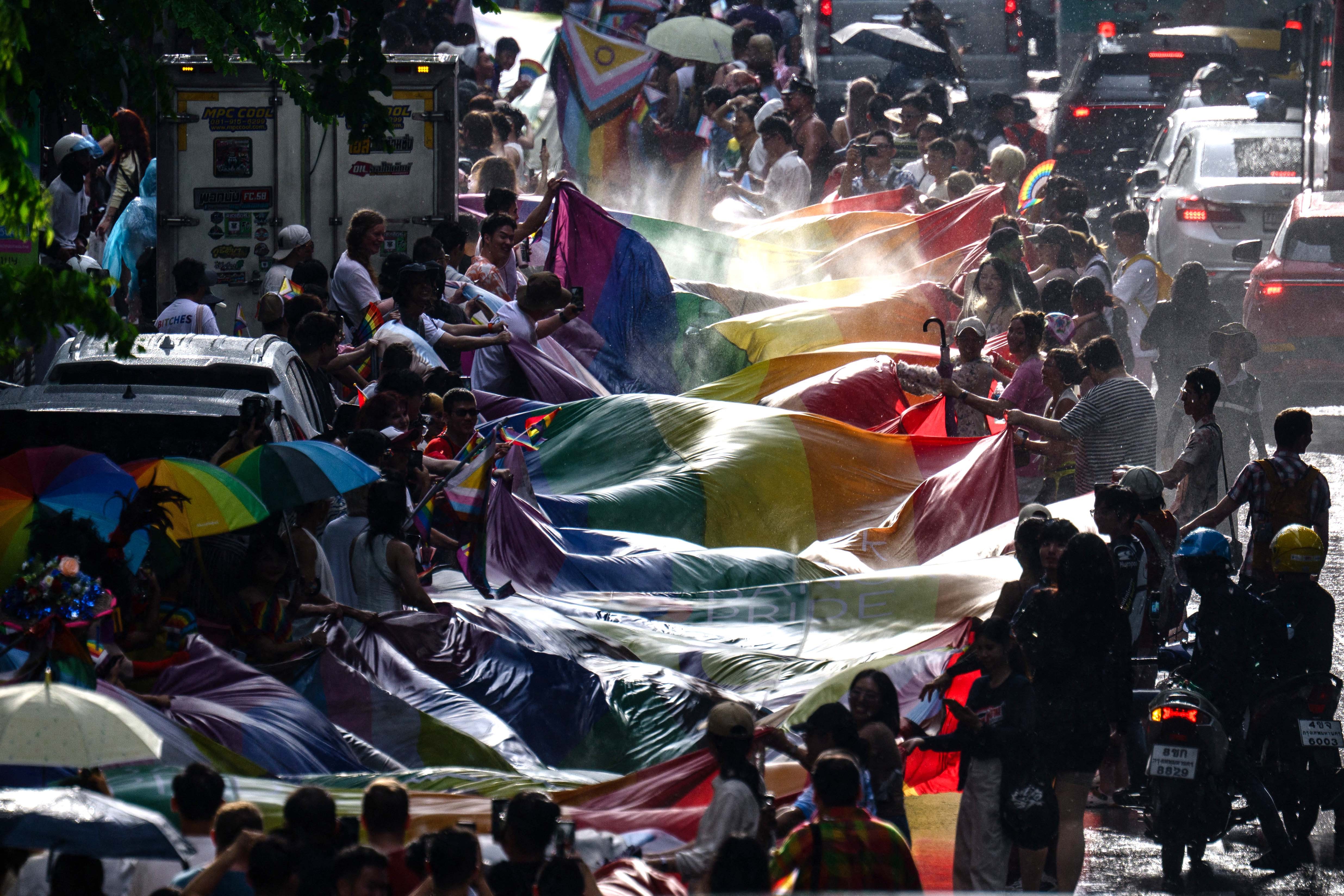 People hold a very long rainbow flag above a street as they take part in a pride parade.