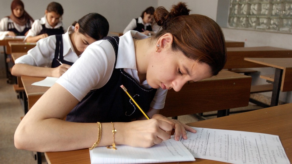 Students in uniform take an exam in a classroom using pencil and paper.