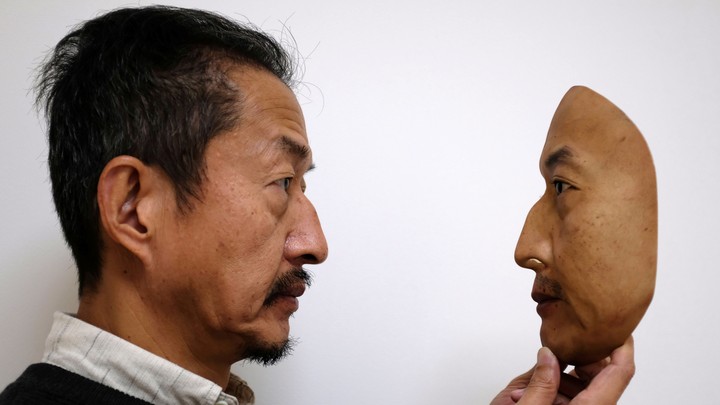 A man holds a realistic replica of a face.