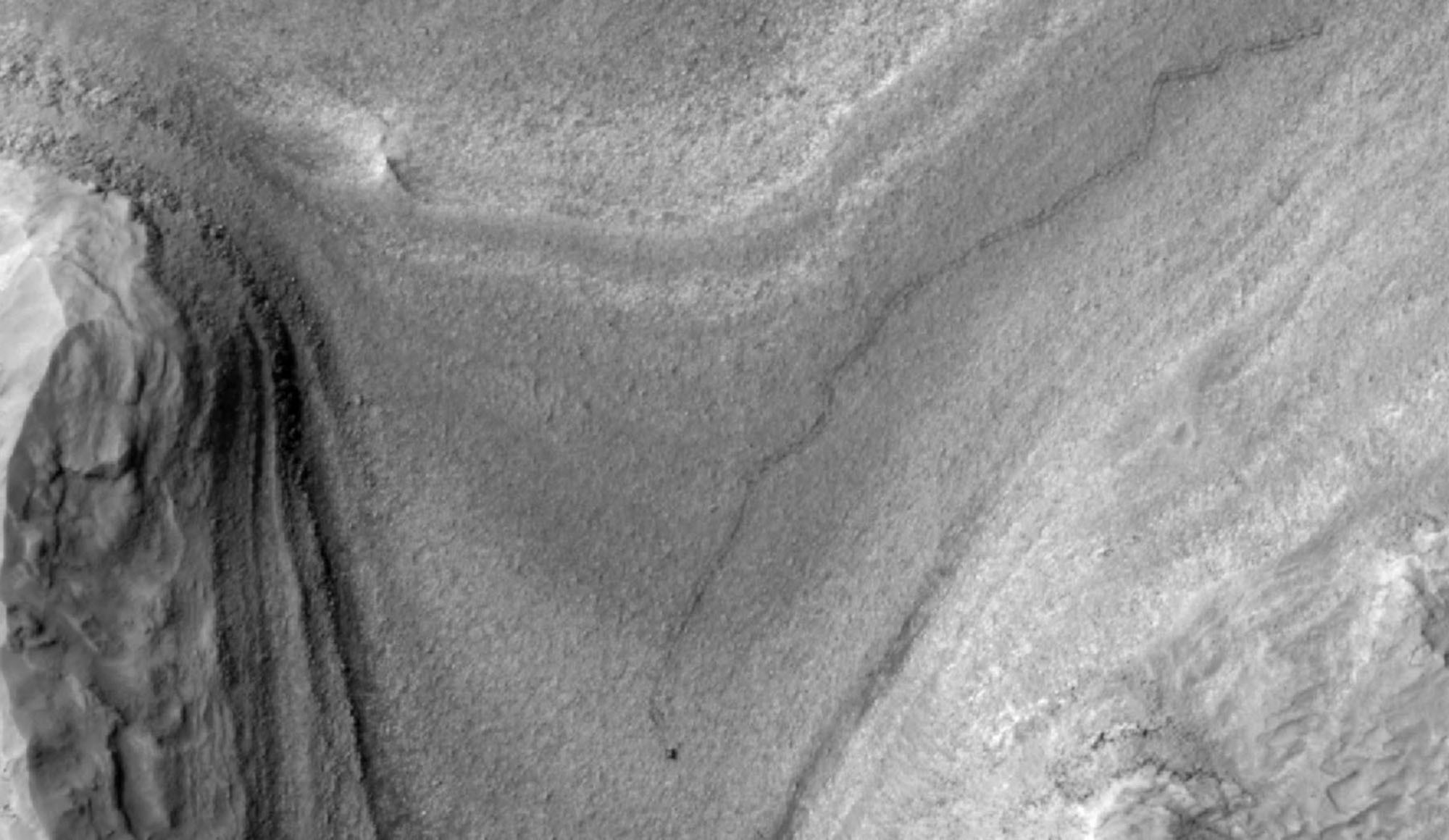 An orbital view of a dusty plain on Mars with wiggly tracks left by a rover