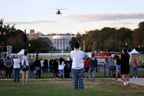 A helicopter flies over the White House as a crowd looks on