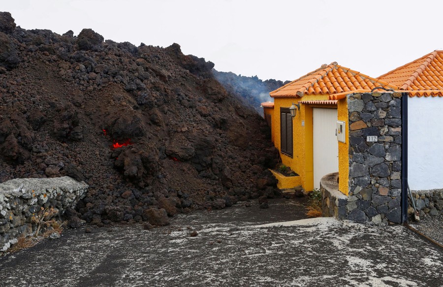 A lava flow fills a road and rests against part of a house.
