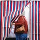 A lady steps into a voting booth with a red white and blue partition