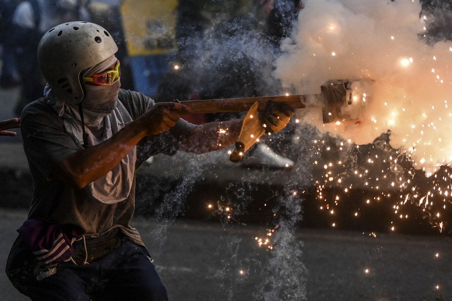 A helmeted protester aims fireworks toward riot police.