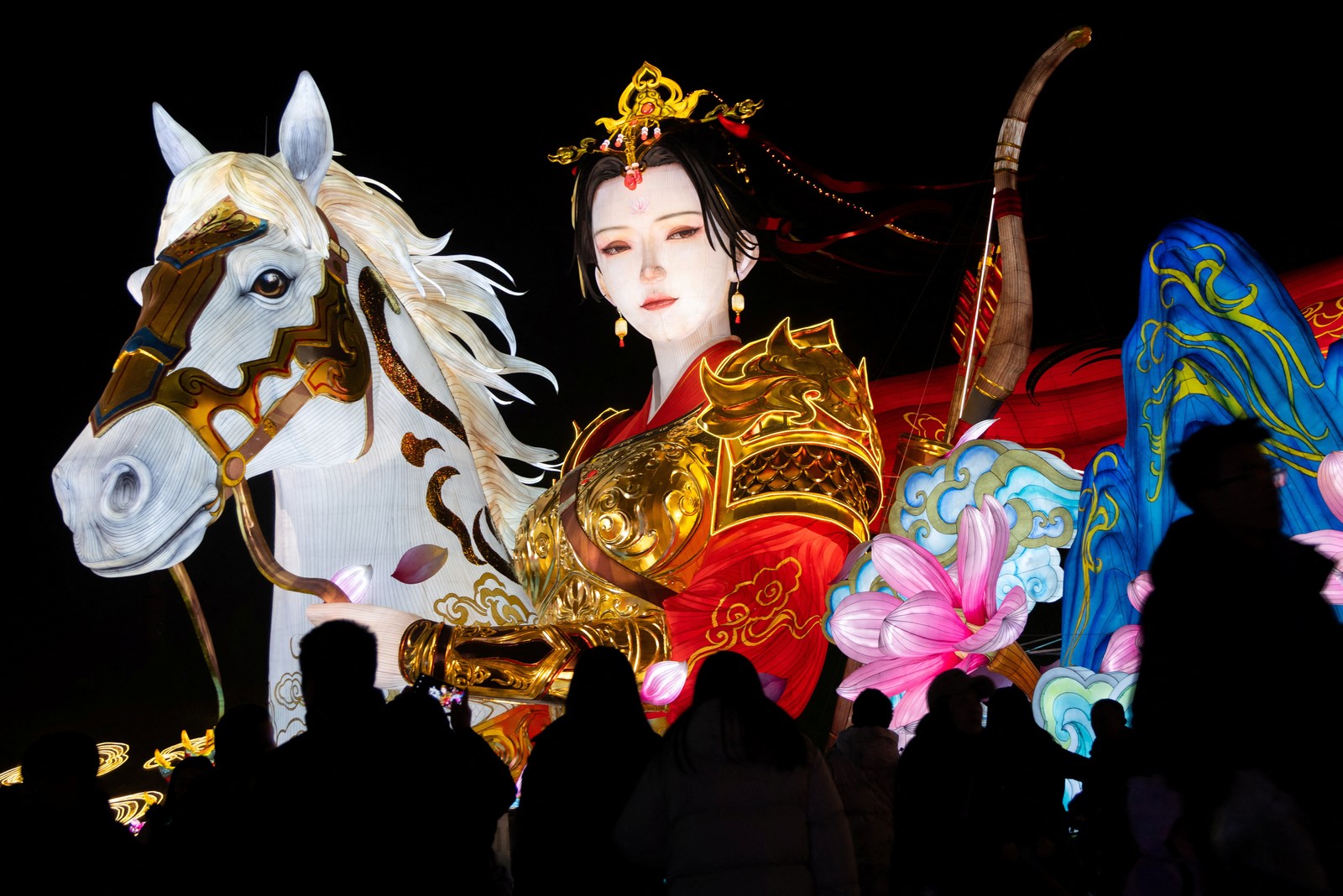 People walk below a large lantern display depicting the legendary warrior Mulan standing beside a horse.