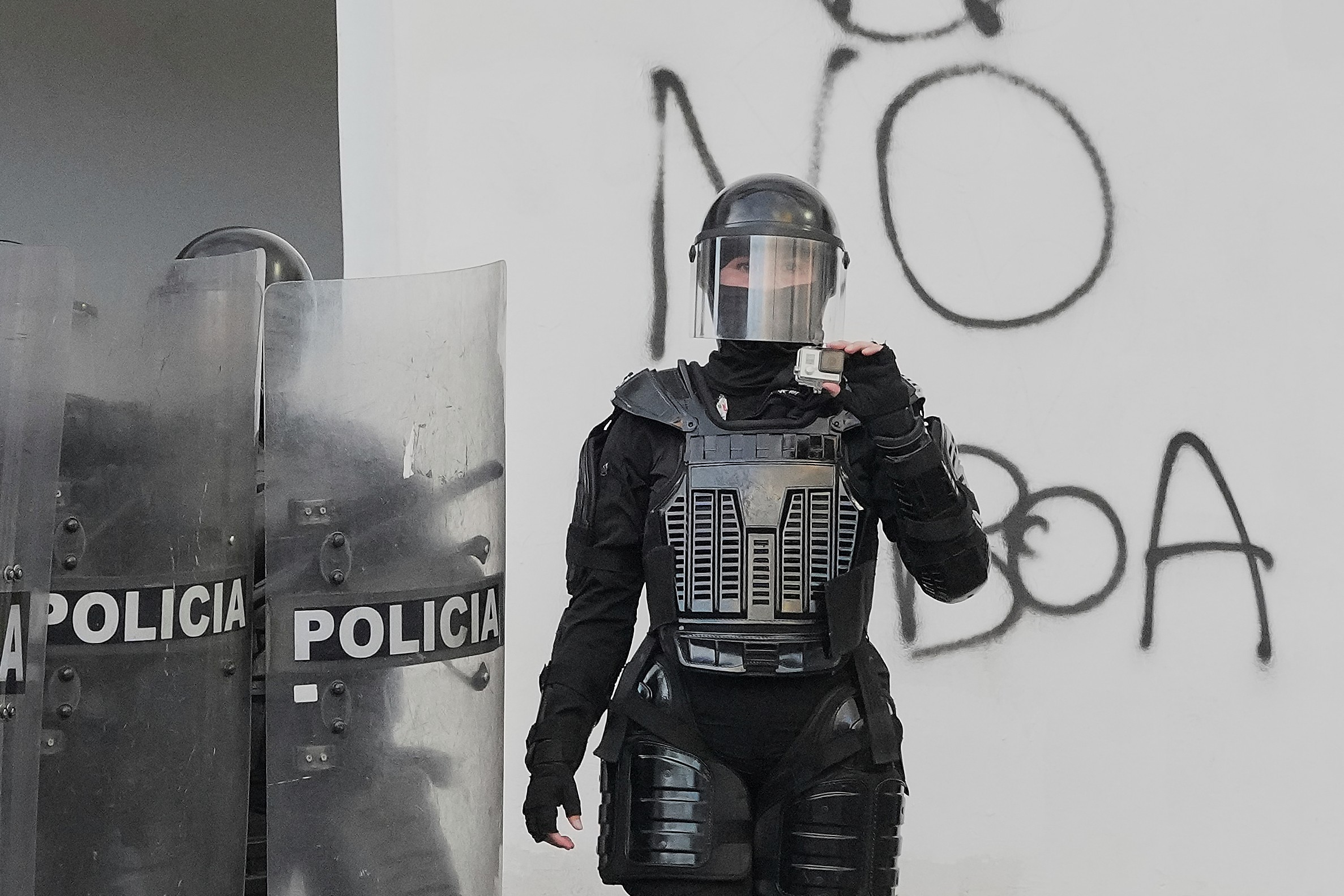 A police officer in riot gear holds up a camera to record protesters.