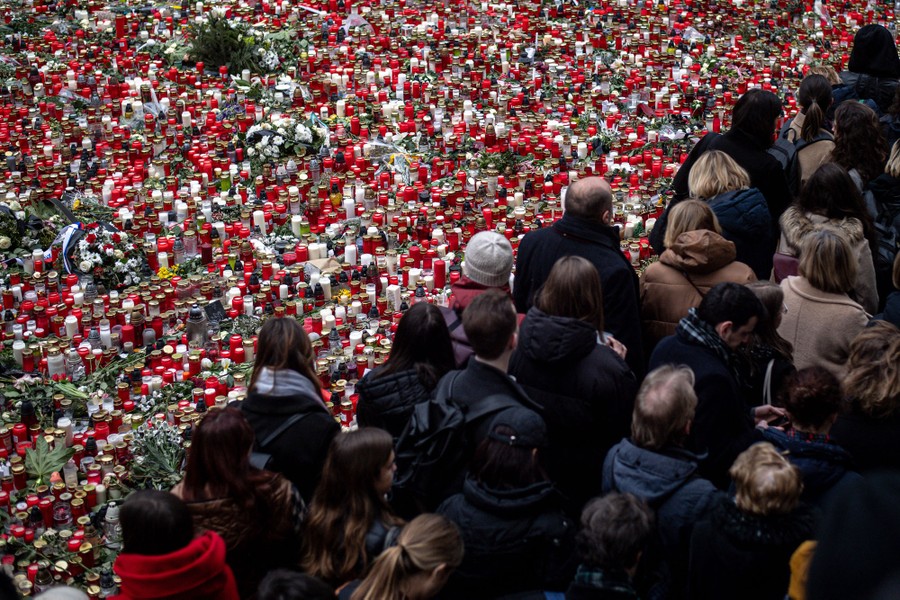 A crowd of people walks past hundreds of candles—a memorial arranged in a city square.