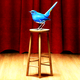 A bluebird perches on a stool onstage in front of red curtains.