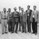 A black and white photograph of Oppenheimer and other scientists at Los Alamos.