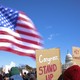 At a protest in front of Capitol Hill, an American flag waves and a sign reads: "Congress, STAND UP"