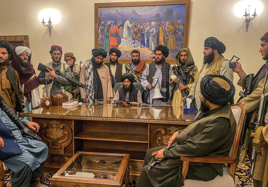 photo of group of men, many carrying weapons, sitting and standing around an ornate wooden desk