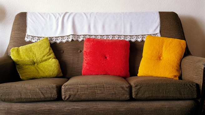 A brown couch with three throw pillows—one green, one red, one yellow—and a white blanket on the back