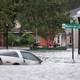 a car is submerged in water in a flooded street while people paddle past it in a canoe