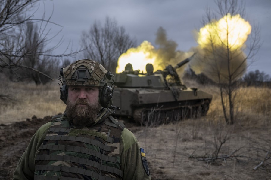 A soldier stands near a mobile artillery unit as it fires.