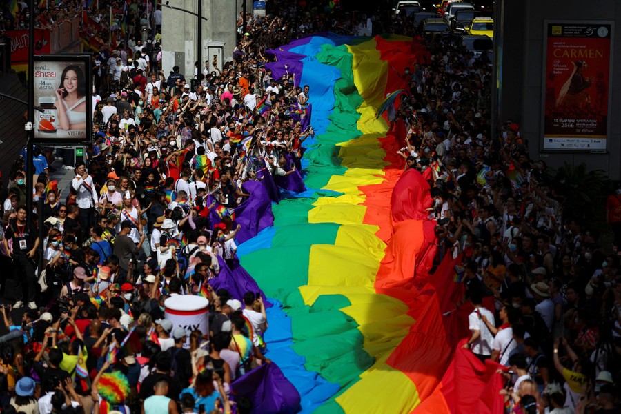 People carry a giant rainbow flag during a Pride parade in a street.