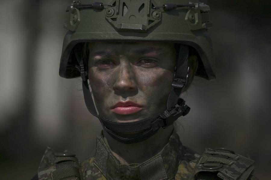A soldier wearing a helmet and camouflage makeup stands guard.
