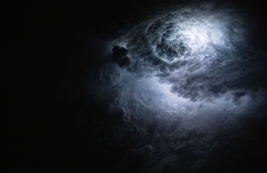 A flash of lightning illuminates storm clouds from within, seen from orbit.