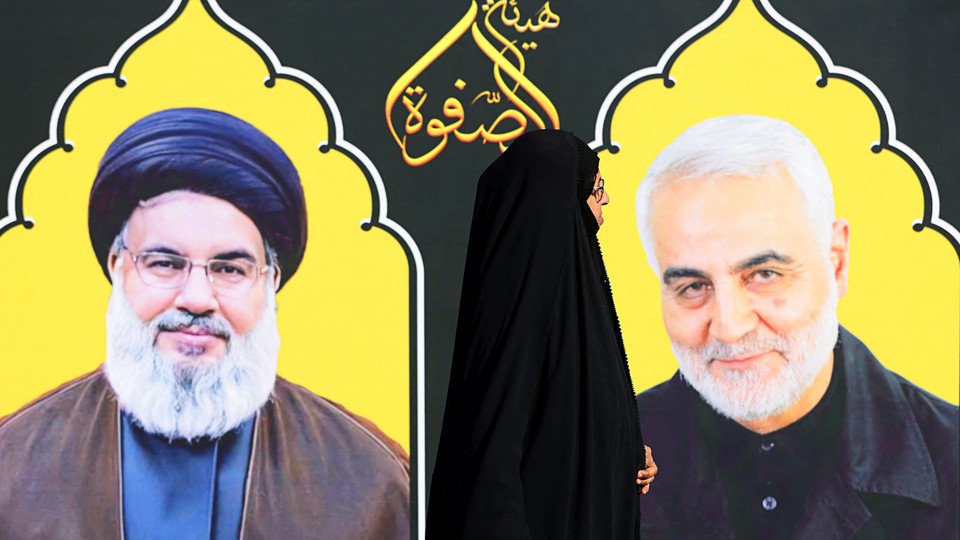 in Baghdad. a woman in hijab walks past portraits of the late Hezbollah leader Hassan Nasrallah and Iranian commander Qasem Soleimani.