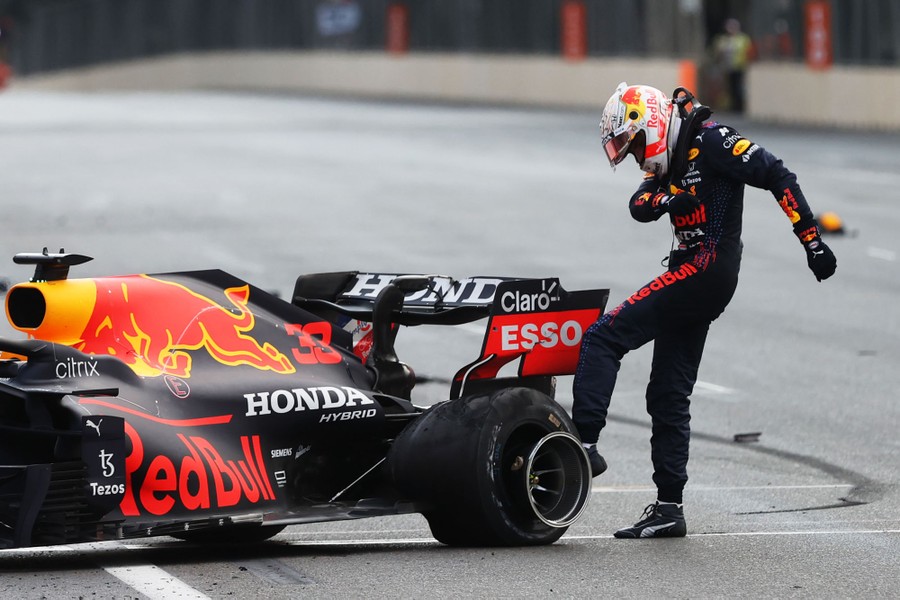 A race car driver kicks the tire of his wrecked car on a racetrack.