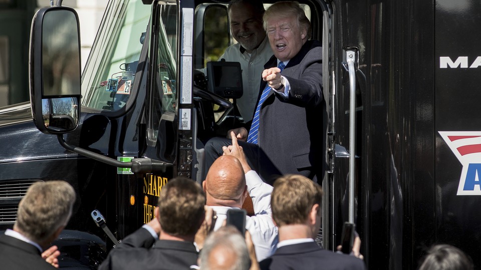 President Donald Trump points to a crowd of men from the driver's seat of a large truck on the south lawn of the White House