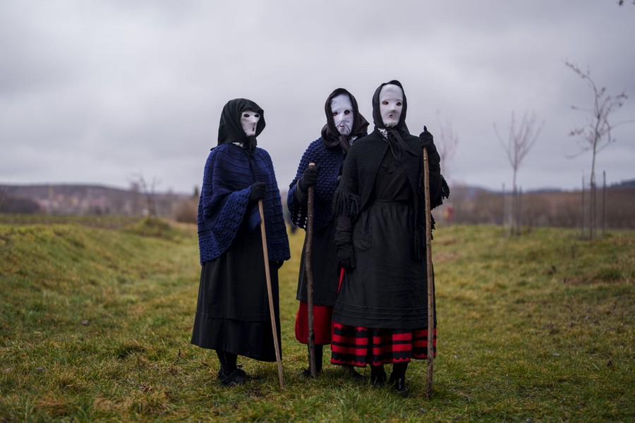 Three people pose for a photo, wearing traditional costumes and masks, standing in a field.