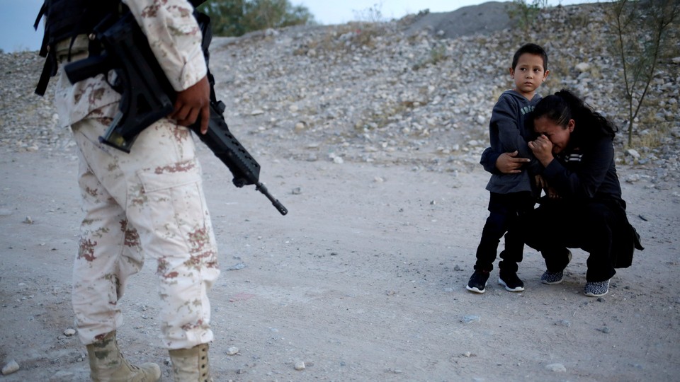 Guatemalan migrant Ledy Perez embraces her son Anthony on a dirt road as a member of the Mexican National Guard stands beside them.