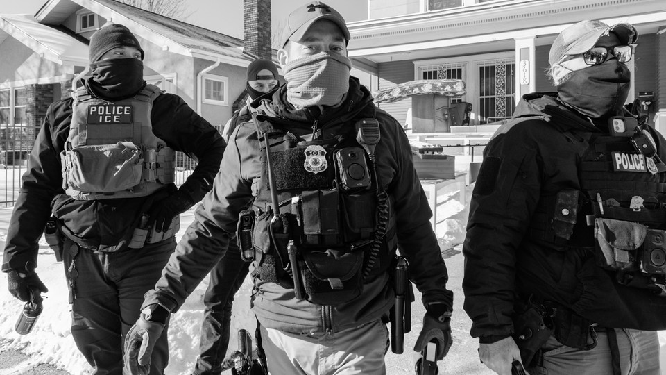 Black-and-white photograph of four ICE agents wearing caps and face masks on a sidewalk in a suburban neighborhood